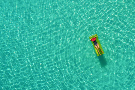 Aerial view of slim woman swimming on the swim mattress in the transparent turquoise sea in...