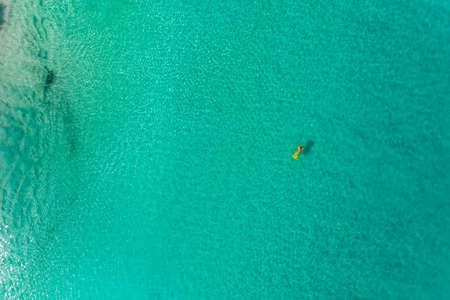 Aerial view of slim woman swimming on the swim mattress in the transparent turquoise sea in...