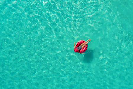 Aerial view of slim woman swimming on the swim ring  donut in the transparent turquoise sea in Seychelles. Summer seascape with girl, beautiful waves, colorful water. Top view from droneの写真素材