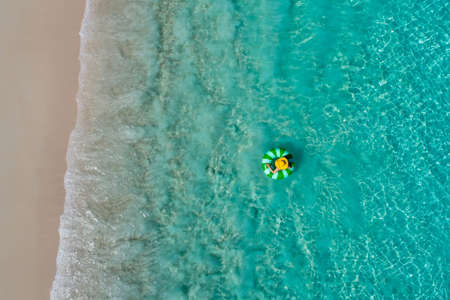 Aerial view of slim woman swimming on the swim ring  donut in the transparent turquoise sea in Seychelles. Summer seascape with girl, beautiful waves, colorful water. Top view from droneの写真素材