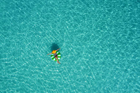 Aerial view of slim woman swimming on the swim ring  donut in the transparent turquoise sea in Seychelles. Summer seascape with girl, beautiful waves, colorful water. Top view from droneの写真素材