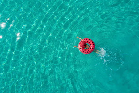 Aerial view of slim woman swimming on the swim ring  donut in the transparent turquoise sea in...