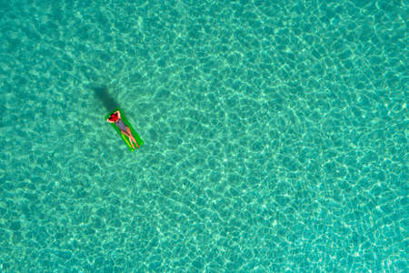 Aerial view of slim woman swimming on the swim mattress in the transparent turquoise sea in Seychelles. Summer seascape with girl, beautiful waves, colorful water. Top view from droneの写真素材