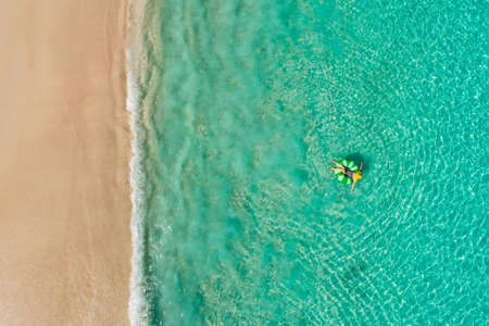 Aerial view of slim woman swimming on the swim ring  donut in the transparent turquoise sea in Seychelles. Summer seascape with girl, beautiful waves, colorful water. Top view from droneの写真素材