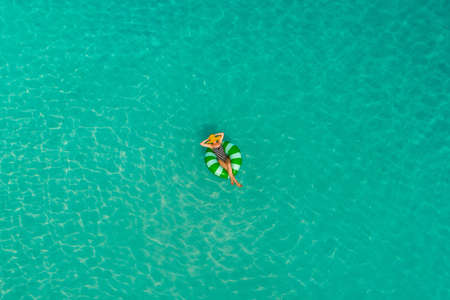 Aerial view of slim woman swimming on the swim ring  donut in the transparent turquoise sea in...