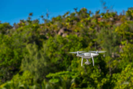 Drone in flight, green trees in the background, selective focus on the drone.