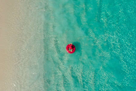Aerial view of slim woman swimming on the swim ring  donut in the transparent turquoise sea in Seychelles. Summer seascape with girl, beautiful waves, colorful water. Top view from droneの写真素材