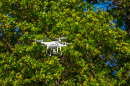 Drone in flight, green trees in the background, selective focus on the drone.