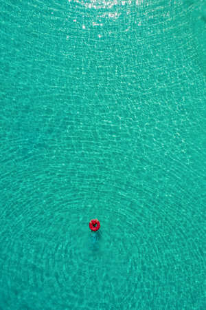 Aerial view of slim woman swimming on the swim ring  donut in the transparent turquoise sea in Seychelles. Summer seascape with girl, beautiful waves, colorful water. Top view from droneの写真素材