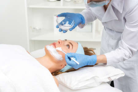 Relaxed young woman is getting facial skin care treatment at beauty salon. Beautician is touching...