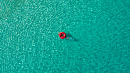Aerial view of slim woman swimming on the swim ring  donut in the transparent turquoise sea in Seychelles. Summer seascape with girl, beautiful waves, colorful water. Top view from droneの写真素材