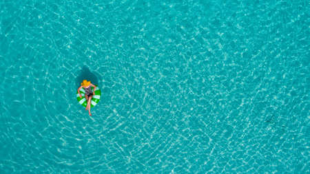 Aerial view of slim woman swimming on the swim ring  donut in the transparent turquoise sea in Seychelles. Summer seascape with girl, beautiful waves, colorful water. Top view from droneの写真素材