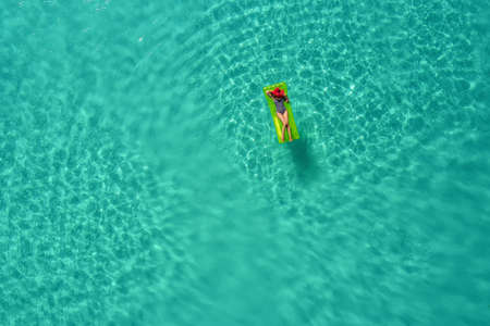 Aerial view of slim woman swimming on the swim mattress in the transparent turquoise sea in...