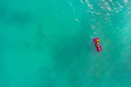 Aerial view of slim woman swimming on the swim mattress in the transparent turquoise sea. Summer seascape with girl, beautiful waves, colorful water. Top view from droneの写真素材