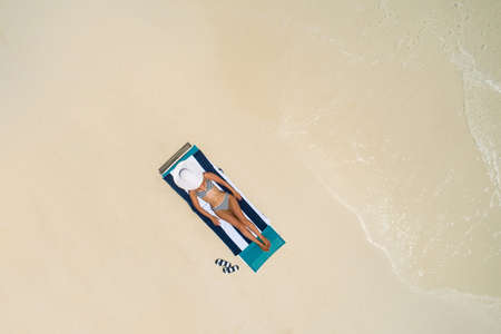Aerial view of slim woman sunbathing lying on a beach chair in Maldives. Summer seascape with girl, beautiful waves, colorful water. Top view from drone.の写真素材