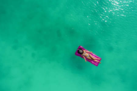 Aerial view of slim woman swimming on the swim mattress in the transparent turquoise sea. Summer seascape with girl, beautiful waves, colorful water. Top view from droneの写真素材