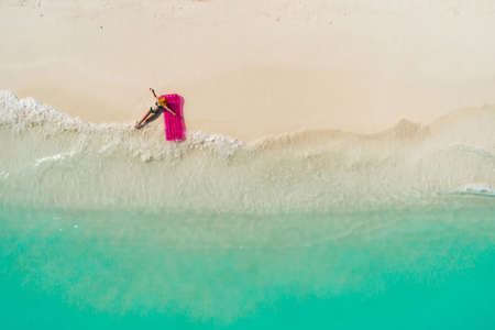 Aerial view of slim woman swimming on the swim mattress in the transparent turquoise sea. Summer seascape with girl, beautiful waves, colorful water. Top view from droneの写真素材