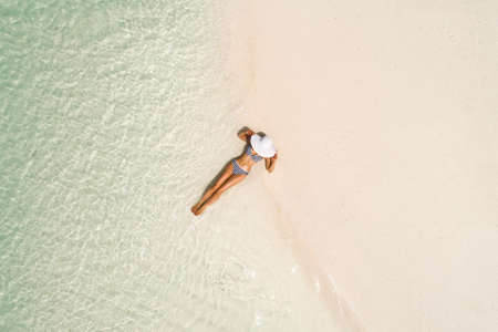 Summer holiday fashion concept - tanning girl wearing sun hat at the beach on a white sand shot from...