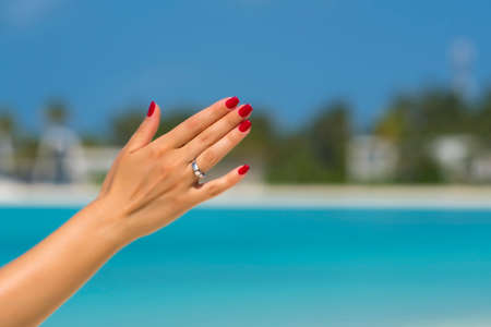 Close up of woman finger showing engagement ring on the tropical beach. Concept of people relationship, ring present, love  and honeymoon at the resort.の写真素材