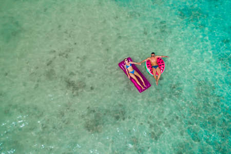 Summer holiday fashion concept - tanning couple at the beach on a turquoise sea shot from above. Top...