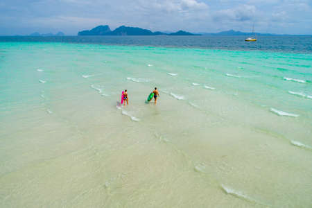 Summer holiday fashion concept - tanning couple at the beach on a turquoise sea shot from above. Top view from drone. Aerial view of slim woman and man sunbathing lying on a beach in Thailand.の写真素材