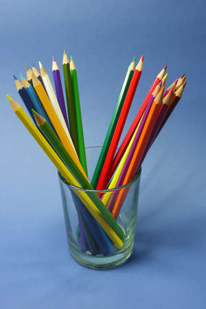 colored pencils in a clear glass beaker on a blue backgroundの写真素材