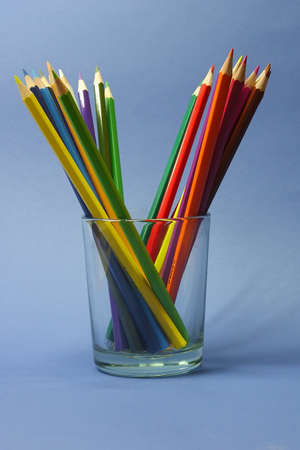 colored pencils in a clear glass beaker on a blue backgroundの写真素材
