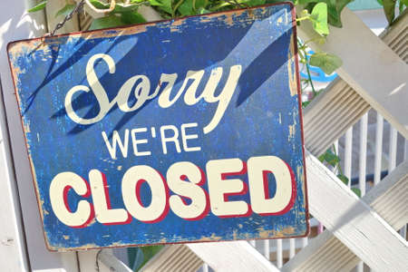A sign written 'Sorry, we're closed' hanging on a white fence.の写真素材