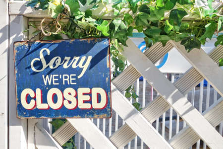 A sign written 'Sorry, we're closed' hanging on a white fence.の写真素材