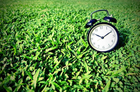 Black vintage clock on green grass.の写真素材