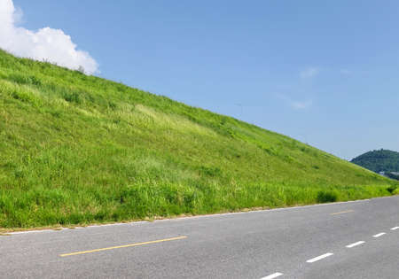 Road with background of slope of green grass and sky.の写真素材