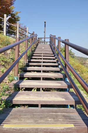 Wooden staircase in outdoor garden. Up hill with blue sky background.