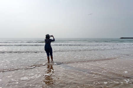 Woman at the beach taking photo with smartphone.の写真素材