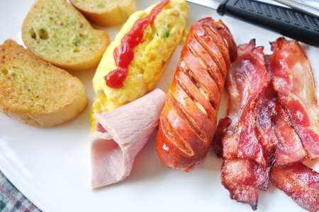 American breakfast, omelette, garlic bread, bacon, ham, sausage on plate.の写真素材