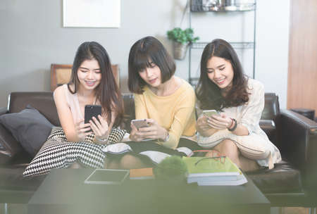 Group of young asian female friends in coffee shop,Using digital devices,chatting with their smartphonesの写真素材