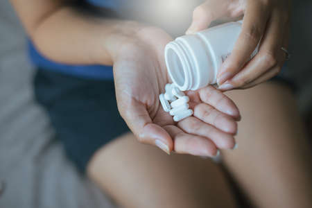 Female hand holding a medicine,Woman hands with pills on spilling pills out of bottleの写真素材