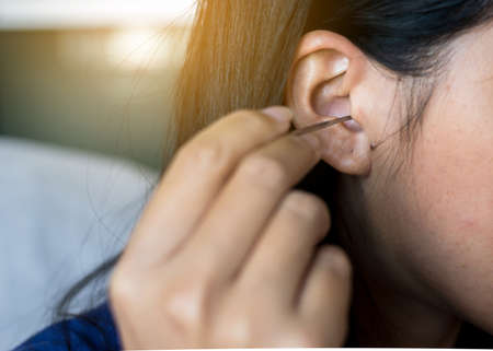 Woman cleaning ear using metal stick,closeupの写真素材