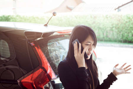 Woman talking on a mobile phone by a broken carの写真素材