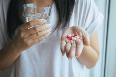 Woman with pills or capsules on hand and a glass of waterの写真素材