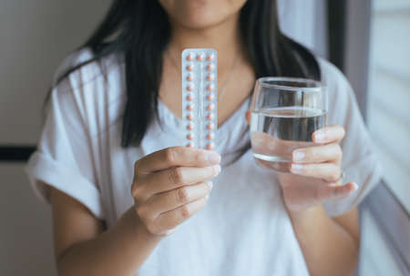 Close up of hand female holding birth control pill and a glass of water,Concept for contraceptionの写真素材