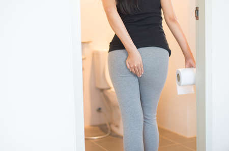 Female holding toilet paper and using toilet in morning,Pants is hanging on her legsの写真素材