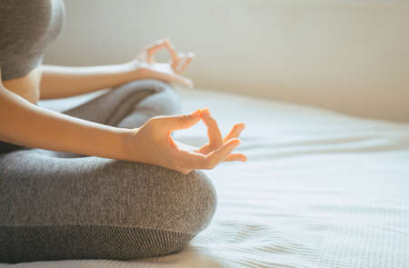 Young asian woman sitting on bed practicing doing yoga meditating,workout after waking up at home,Healthy and  lifestyle conceptの写真素材