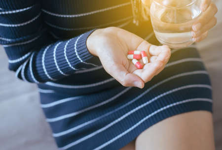 Woman with pills or capsules on hand and a glass of waterの写真素材