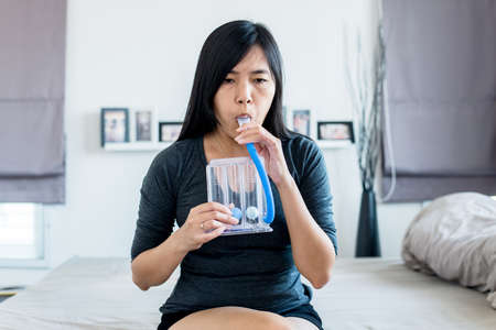 Asian woman patient using incentivespirometer or three balls for stimulate lung at homeの写真素材