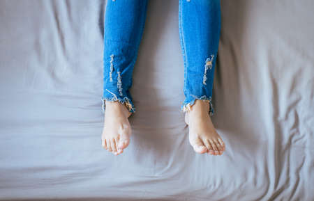 Close up of woman legs with blue jeans,Feet and stretch lazily on the bedの写真素材
