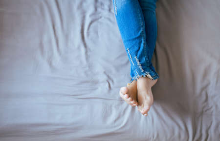 Close up of woman legs with blue jeans,Feet and stretch lazily on the bedの写真素材