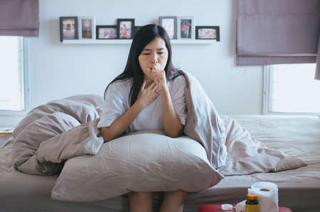 Young asian woman coughing and sitting on her bed,Concept of healthの写真素材