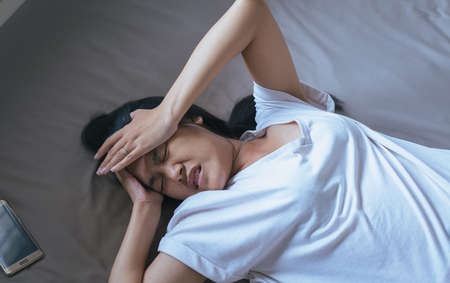 Asian woman have a headache on bed after wake up in the morningの写真素材