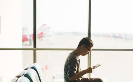 Asian man traveler using mobile phone internet and wifi in airport,Lifestyle using cell phone connection conceptの写真素材