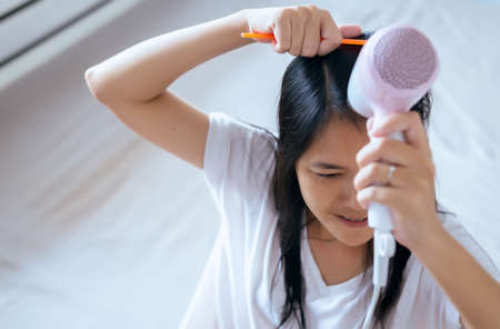 Young asian woman after bath hairbrushing her hair with comb,Female drying her long hair with dryerの写真素材